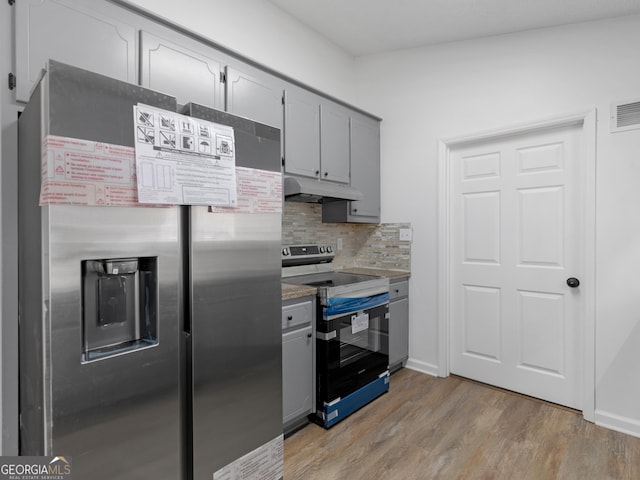 kitchen featuring stainless steel appliances, gray cabinets, light wood-style flooring, backsplash, and under cabinet range hood