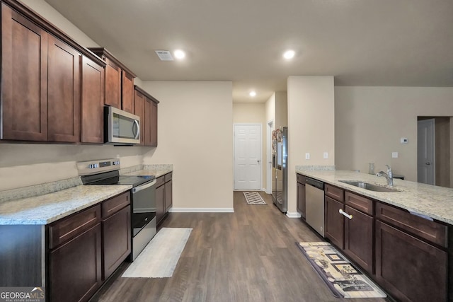 kitchen with baseboards, dark wood finished floors, light stone counters, stainless steel appliances, and a sink