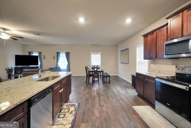 kitchen featuring light stone counters, stainless steel appliances, visible vents, open floor plan, and a sink