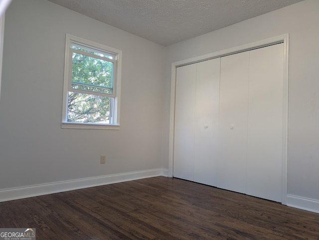 unfurnished bedroom with dark wood-style floors, a textured ceiling, a closet, and baseboards