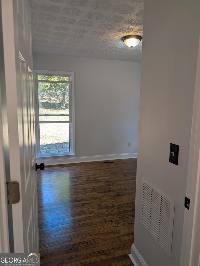 unfurnished room with dark wood-style floors, baseboards, visible vents, and a textured ceiling