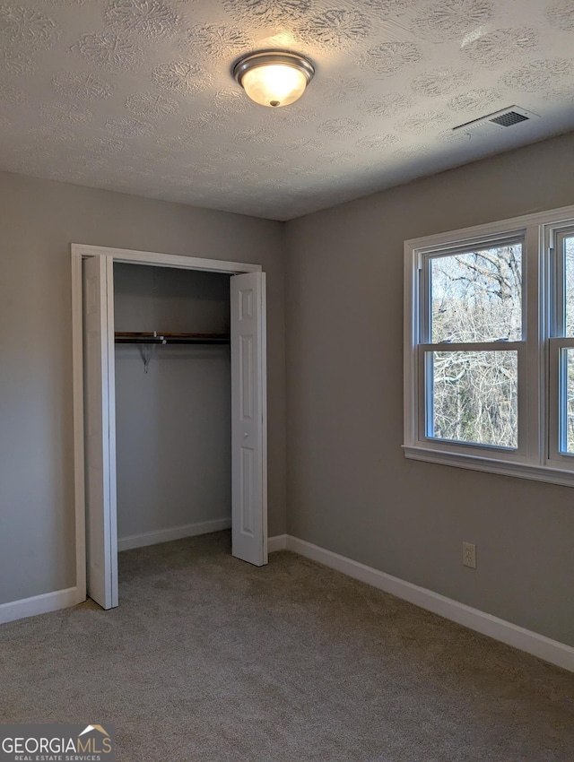 unfurnished bedroom featuring a textured ceiling, carpet flooring, visible vents, baseboards, and a closet