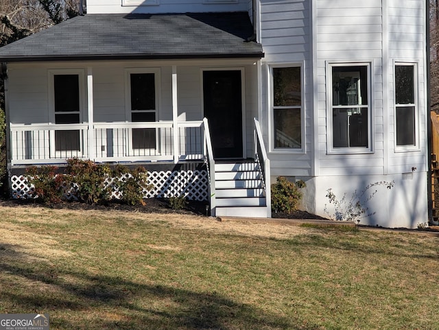 view of exterior entry with roof with shingles, a porch, and a lawn