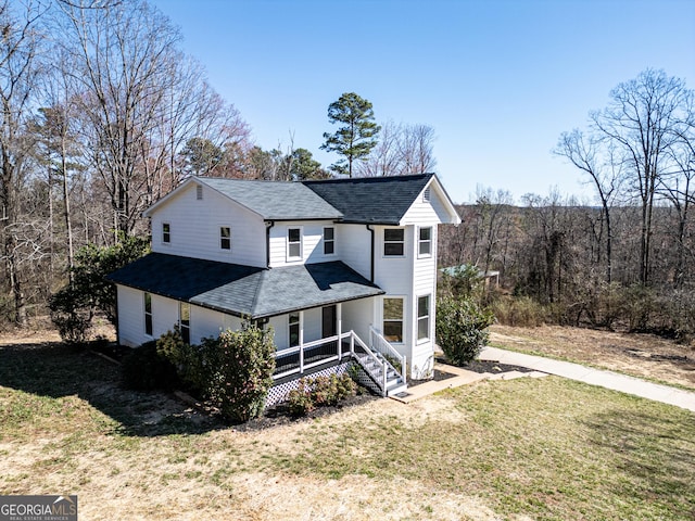 entrance to property featuring covered porch, roof with shingles, and a yard