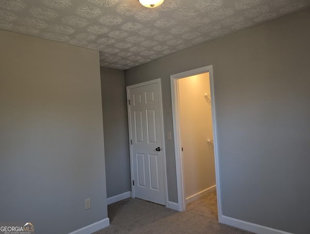 unfurnished bedroom with a textured ceiling, a spacious closet, baseboards, and carpet flooring