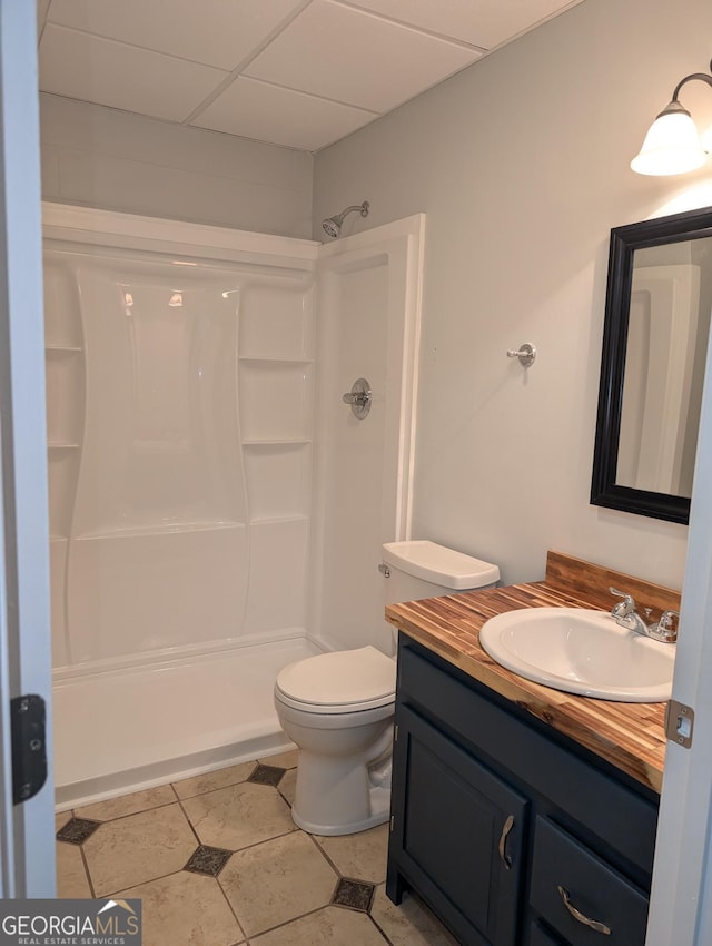 bathroom with toilet, a shower, a drop ceiling, and vanity