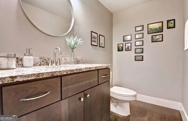 half bathroom featuring toilet, baseboards, wood finished floors, and vanity