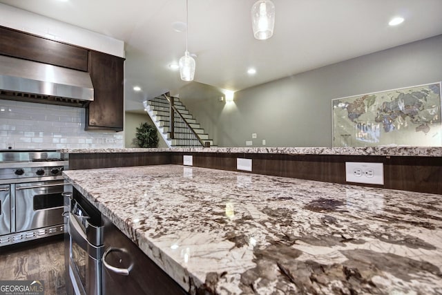 kitchen with pendant lighting, tasteful backsplash, high end stainless steel range oven, dark brown cabinets, and light stone countertops