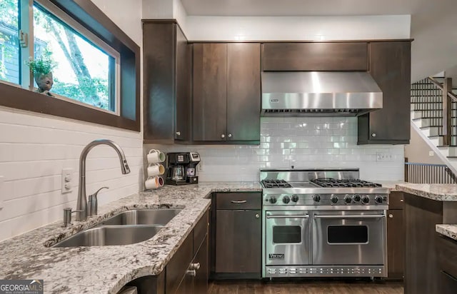 kitchen featuring wall chimney range hood, double oven range, dark brown cabinets, and a sink