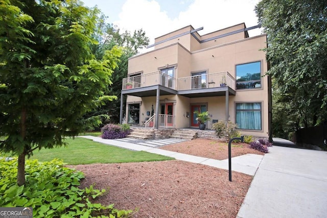 back of house with a lawn, a balcony, and stucco siding