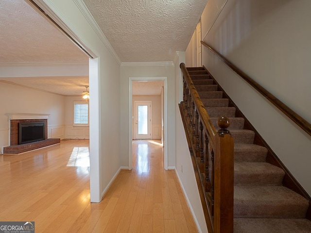 stairs featuring ornamental molding, a fireplace, a textured ceiling, and wood finished floors