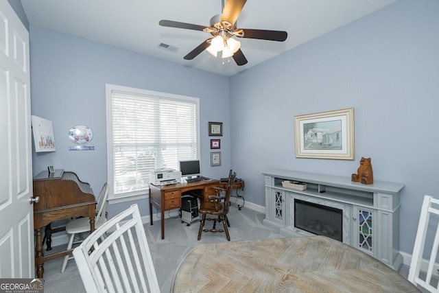 office area featuring ceiling fan, light carpet, a fireplace, visible vents, and baseboards