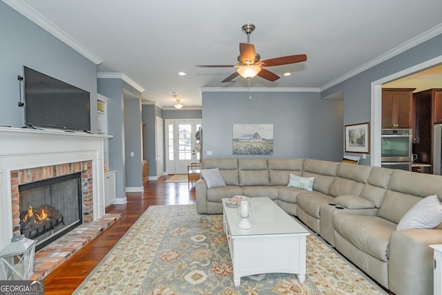 living area with baseboards, wood finished floors, crown molding, a brick fireplace, and recessed lighting