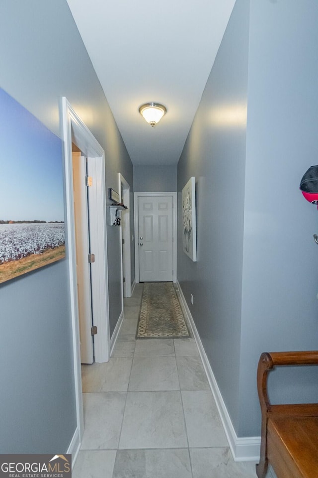 hall featuring light tile patterned flooring and baseboards