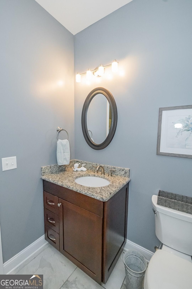 half bathroom with toilet, marble finish floor, vanity, and baseboards