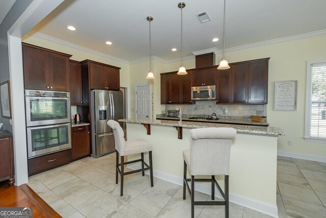 kitchen featuring a center island with sink, crown molding, stainless steel appliances, backsplash, and a kitchen bar