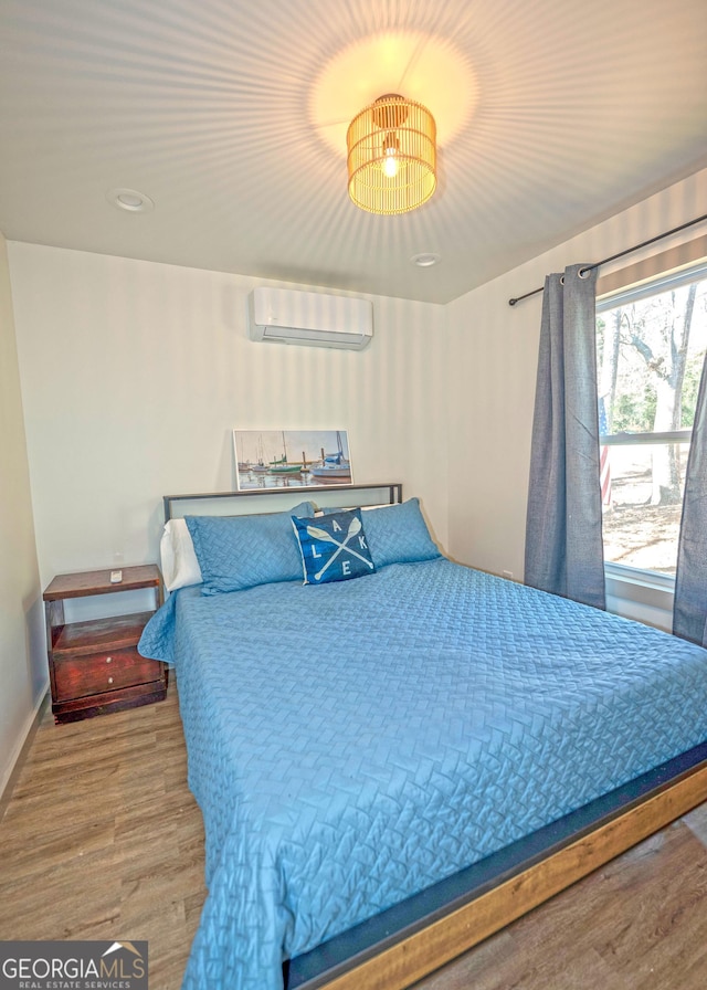 bedroom featuring a wall unit AC, baseboards, and wood finished floors