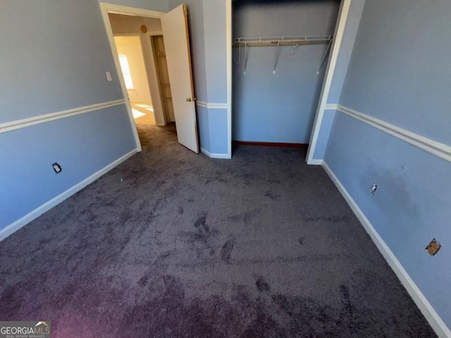 unfurnished bedroom with baseboards, dark colored carpet, and a closet