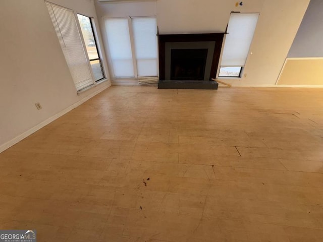 unfurnished living room with light wood-style floors, a fireplace with raised hearth, and baseboards