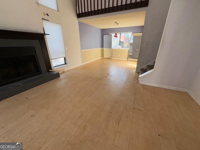 unfurnished living room featuring light wood-type flooring, a fireplace with raised hearth, a high ceiling, and baseboards