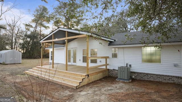 rear view of property featuring an outbuilding, a storage unit, a shingled roof, central air condition unit, and a wooden deck