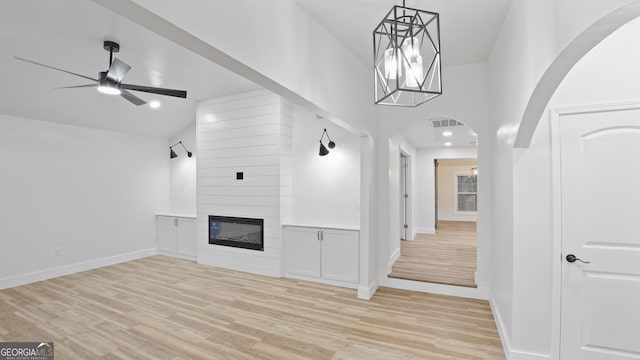 unfurnished living room with ceiling fan with notable chandelier, a fireplace, light wood-style flooring, and baseboards