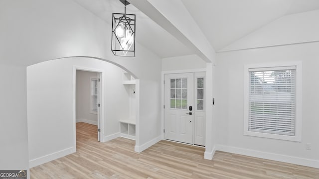 foyer featuring arched walkways, baseboards, lofted ceiling, and light wood-style floors