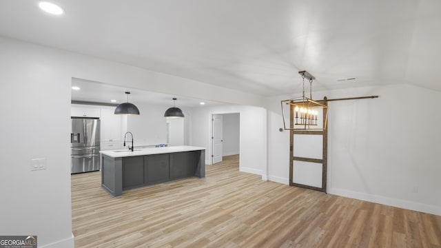 kitchen with white cabinets, light countertops, an island with sink, stainless steel fridge, and decorative light fixtures