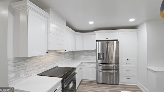 kitchen with black range with electric cooktop, light countertops, backsplash, white cabinetry, and stainless steel fridge