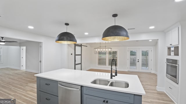 kitchen with a barn door, white cabinets, appliances with stainless steel finishes, light countertops, and a sink