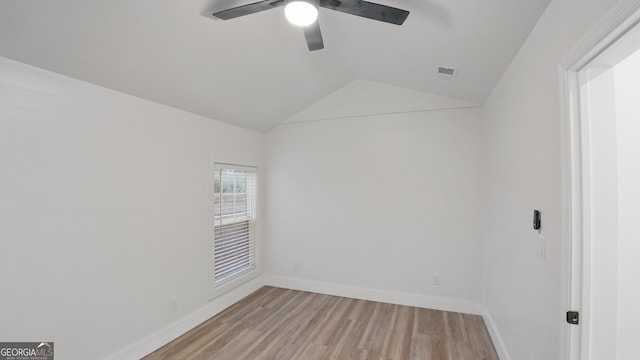 spare room featuring baseboards, visible vents, a ceiling fan, light wood-style flooring, and vaulted ceiling