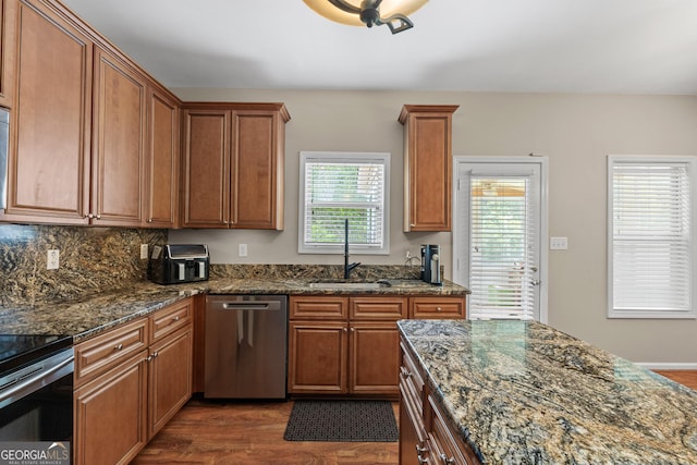 kitchen with appliances with stainless steel finishes, brown cabinets, dark wood-type flooring, dark stone countertops, and a sink