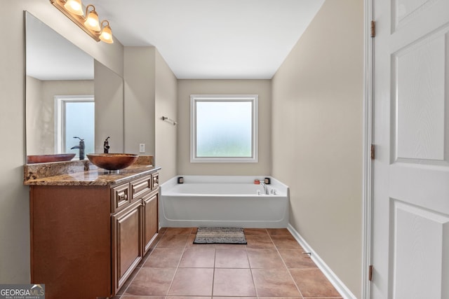 bathroom with a garden tub, vanity, baseboards, and tile patterned floors