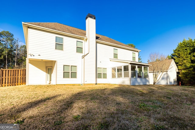 back of property featuring a lawn, a chimney, fence, and a sunroom