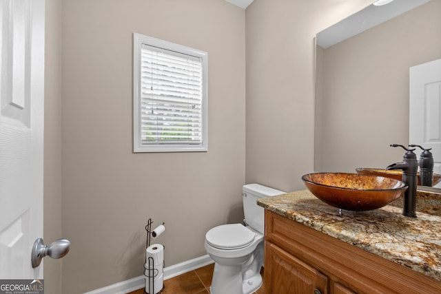 half bath with toilet, tile patterned flooring, vanity, and baseboards