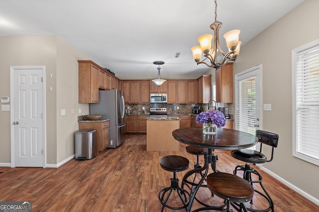 kitchen featuring baseboards, dark wood finished floors, decorative backsplash, a kitchen island, and appliances with stainless steel finishes