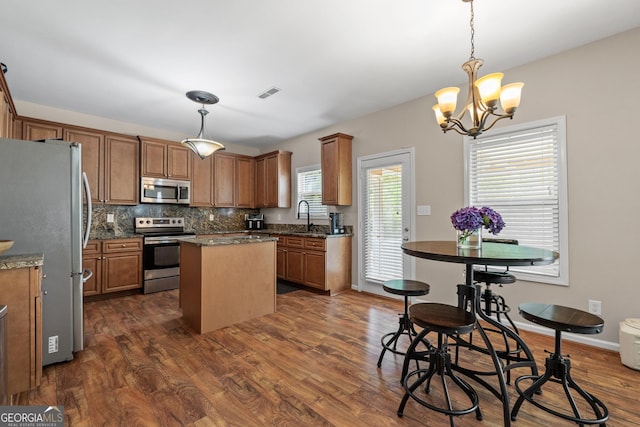 kitchen featuring dark wood-style floors, brown cabinets, stainless steel appliances, backsplash, and a kitchen island