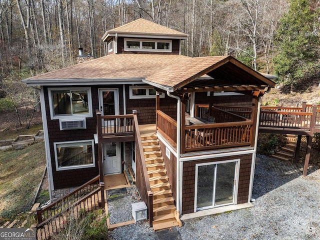 view of front of house with stairs, a wooded view, and roof with shingles