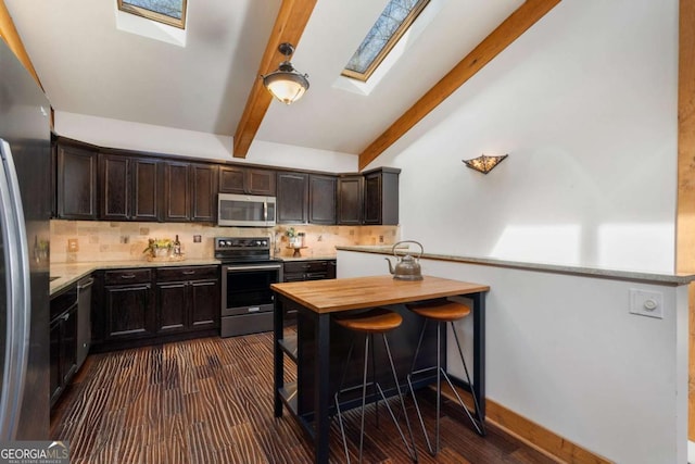 kitchen featuring appliances with stainless steel finishes, vaulted ceiling with skylight, backsplash, and dark brown cabinets