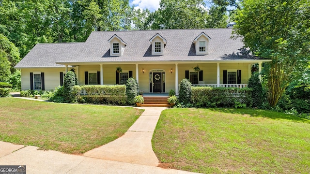 cape cod-style house with a shingled roof, a front yard, and covered porch