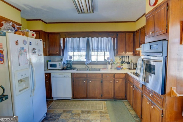 kitchen featuring light countertops, white appliances, brown cabinetry, and a sink