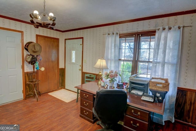 home office featuring a chandelier, light wood-style flooring, ornamental molding, wainscoting, and wallpapered walls