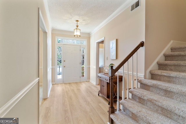 foyer entrance with light wood-style flooring, a textured ceiling, visible vents, and a wealth of natural light