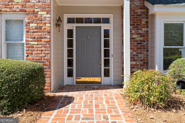 entrance to property with a shingled roof and brick siding