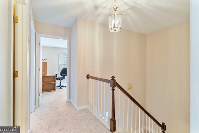 hallway with a chandelier, carpet flooring, an upstairs landing, and baseboards