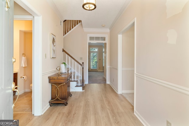 foyer entrance with ornamental molding, light wood-style floors, stairway, and baseboards