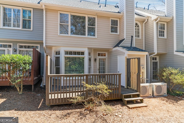 rear view of house with ac unit, a chimney, a deck, and roof with shingles