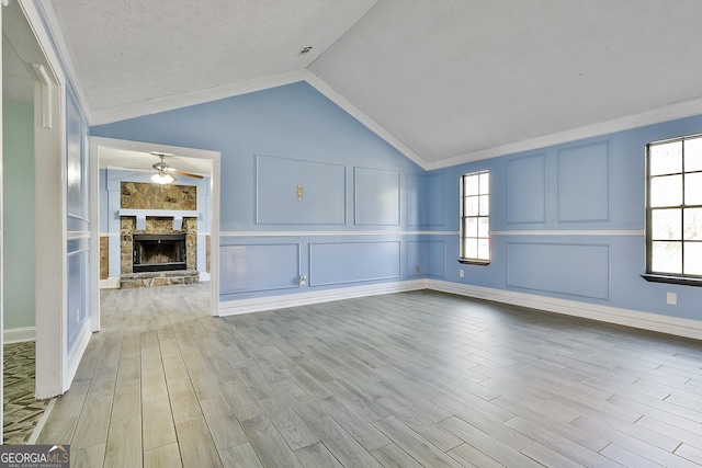 unfurnished living room with lofted ceiling, a stone fireplace, light wood-style floors, and a decorative wall