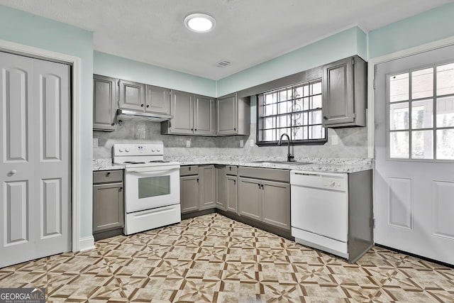 kitchen with white appliances, gray cabinets, light countertops, under cabinet range hood, and a sink