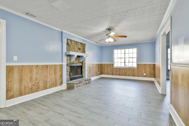 unfurnished living room with a wainscoted wall, a fireplace, visible vents, and a textured ceiling